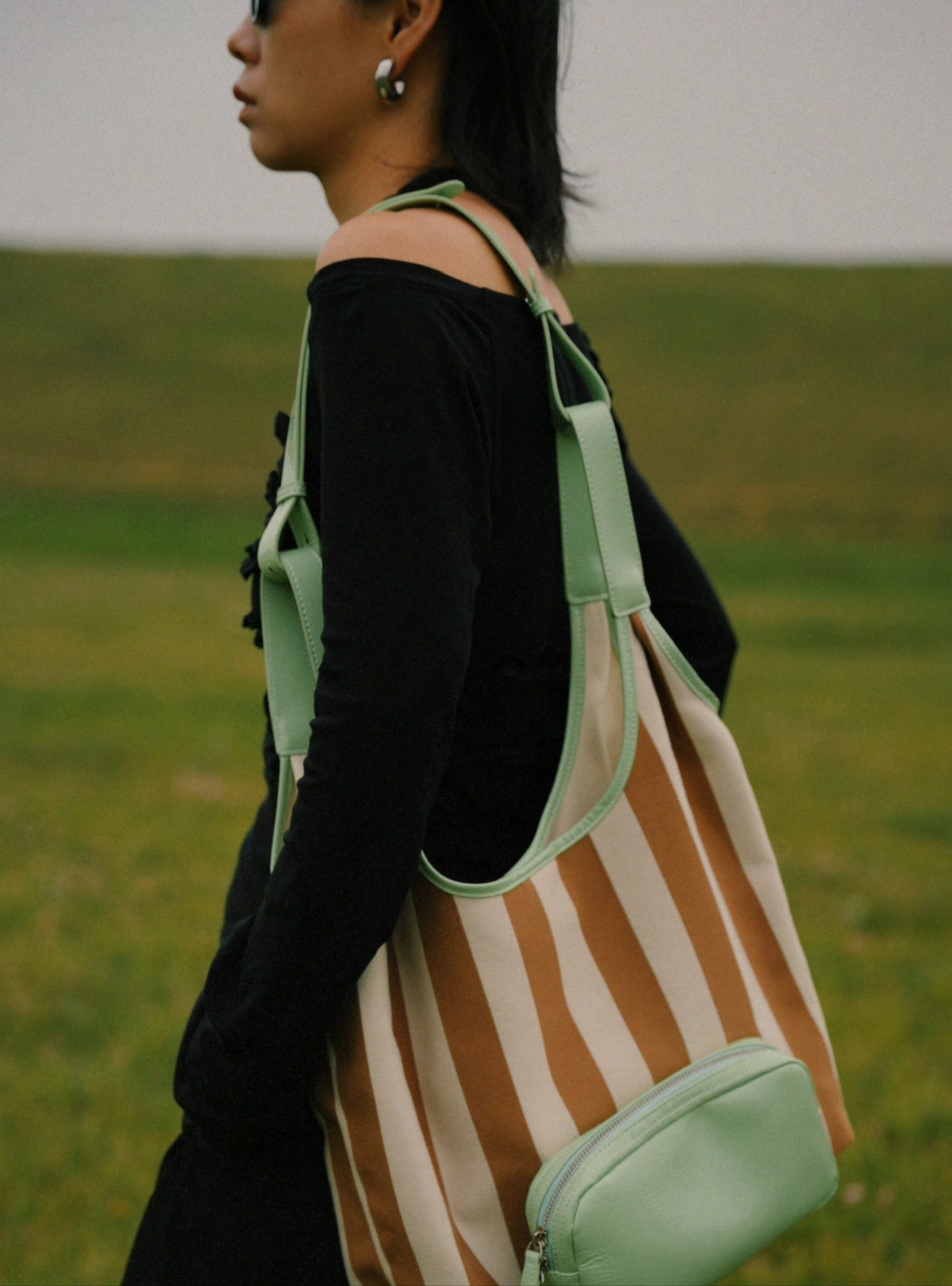 Person wearing a striped bag with a green strap in an outdoor setting