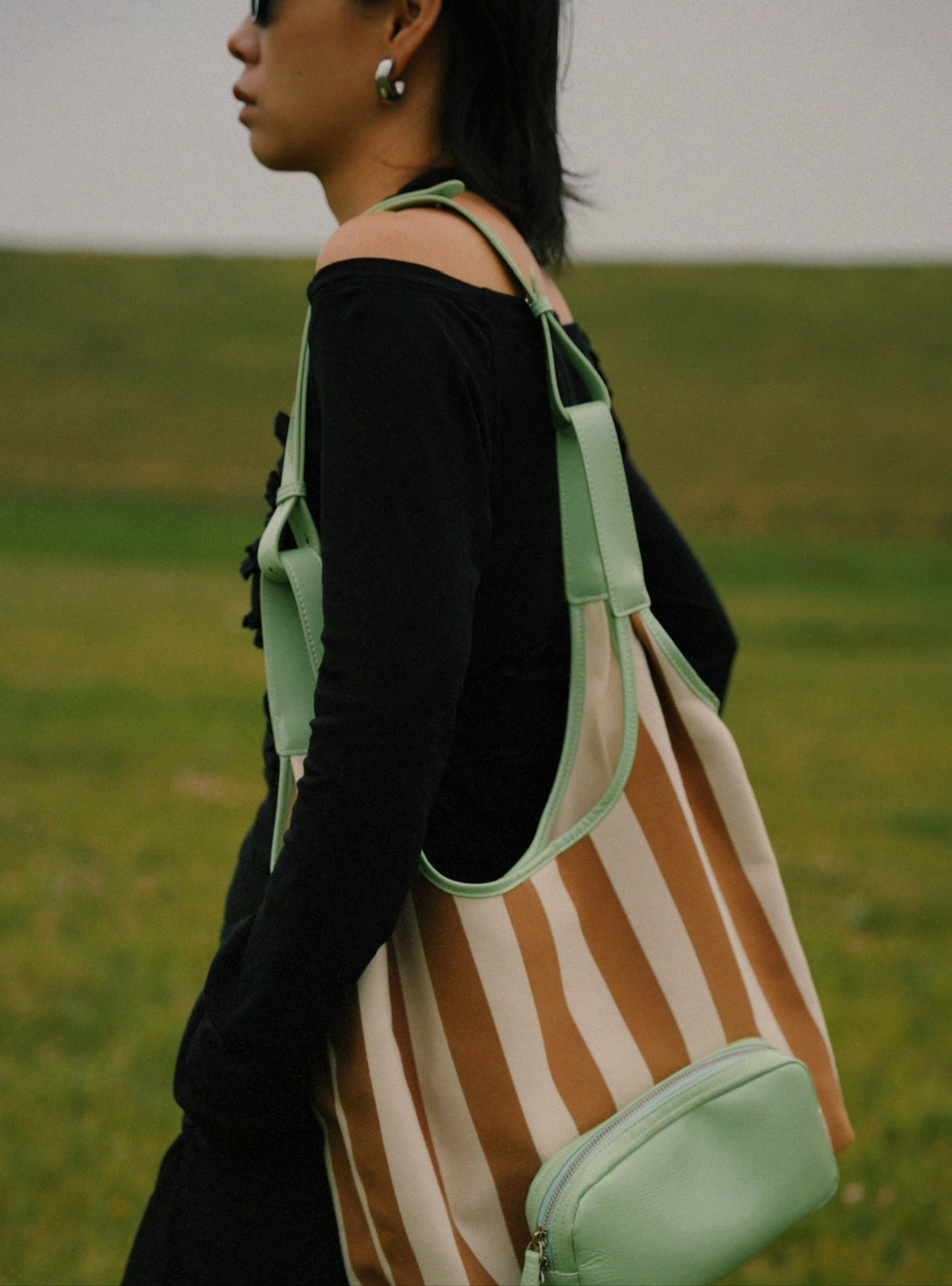 Person wearing a striped bag with a green strap in an outdoor setting