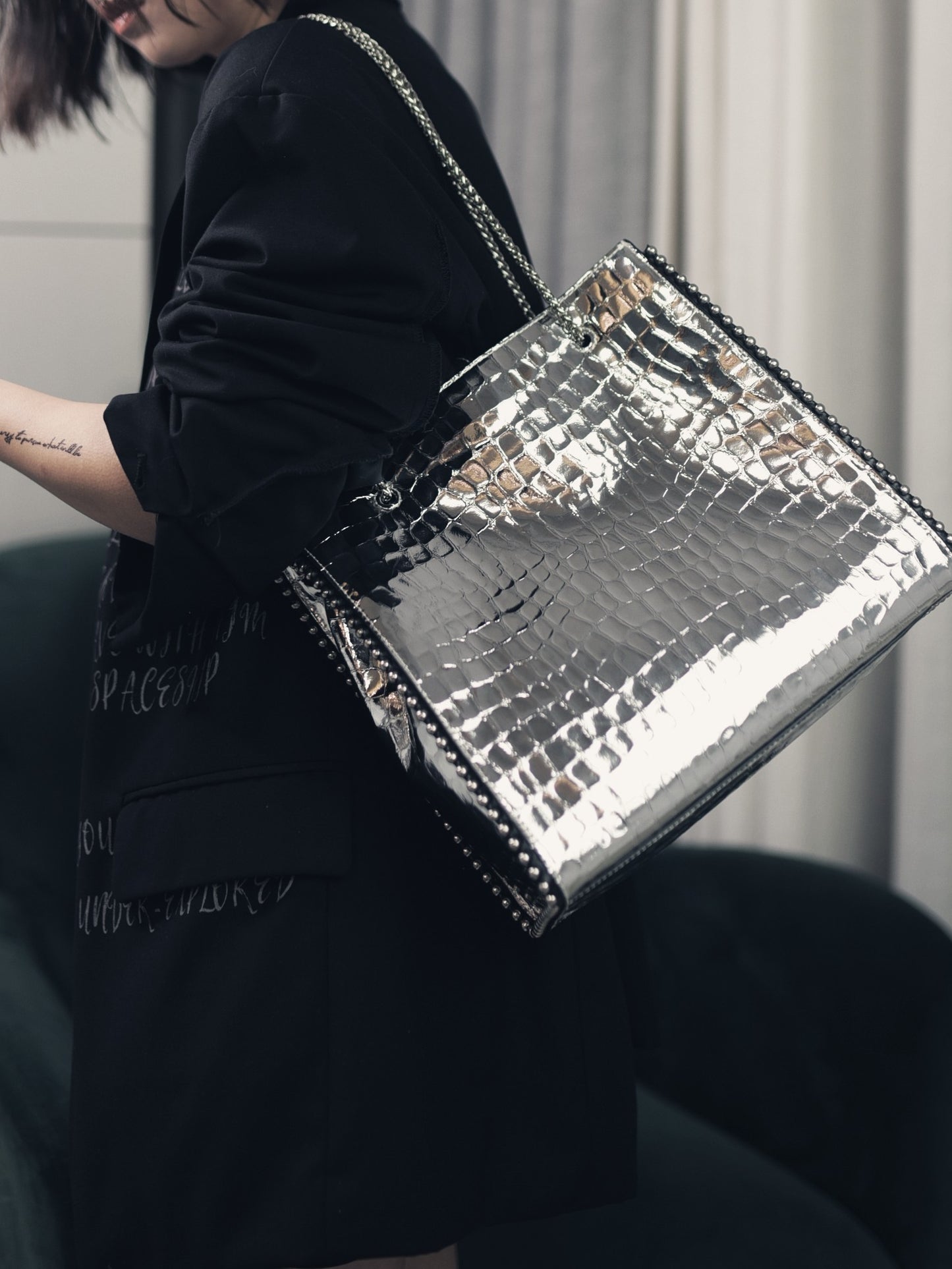 Silver metallic handbag held by a person wearing a black outfit.